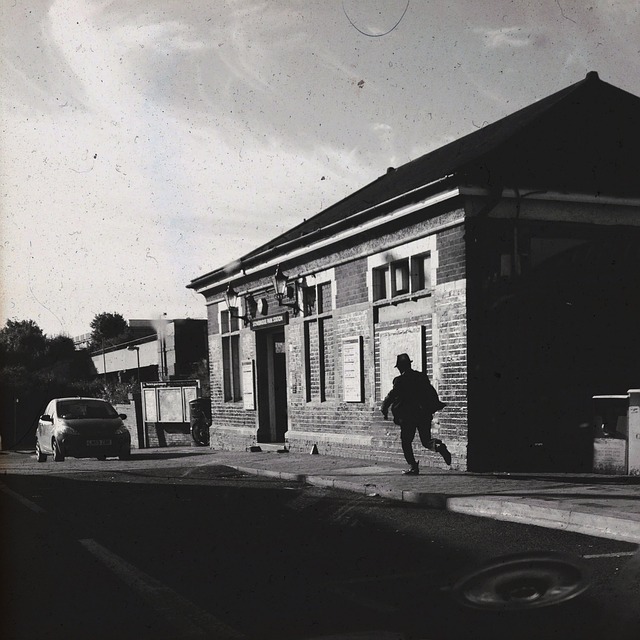 muž běžící po ulici ke dveřím budovy, černobílá fotografie